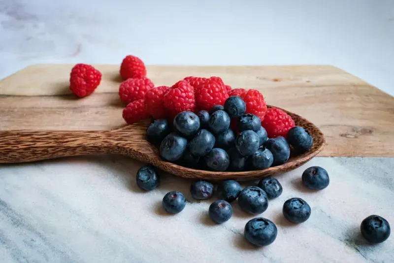 a picture of blueberries and raspberries on a wooden spoon